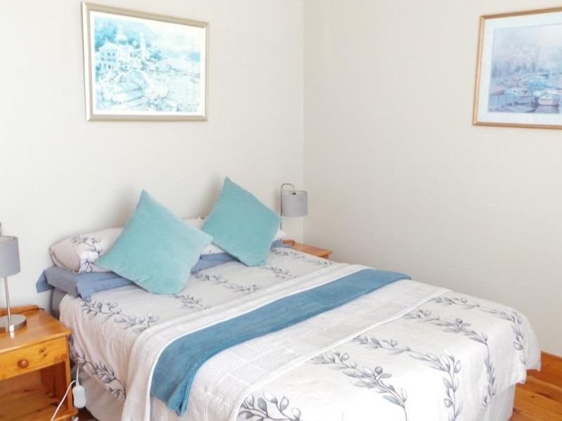 A cozy bedroom featuring warm timber flooring and wall-mounted lighting, providing a comfortable and inviting sleeping space.