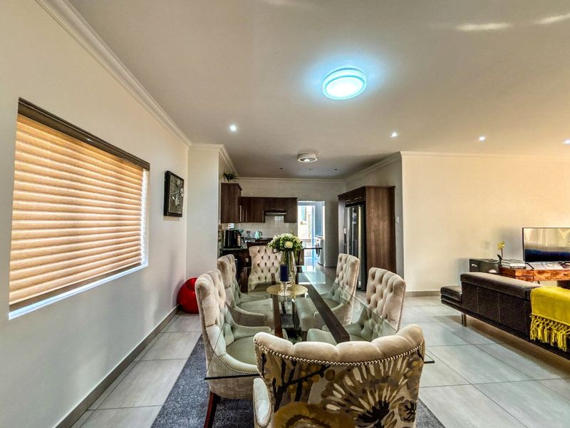 An open-plan living and dining area featuring tiled flooring, recessed lighting, and a modern kitchen with built-in cabinetry and integrated appliances.