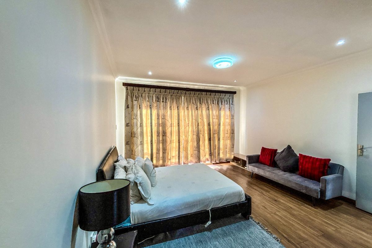 A spacious bedroom featuring laminate flooring, recessed downlighting, and large window treatments, offering a comfortable and well-maintained living space.