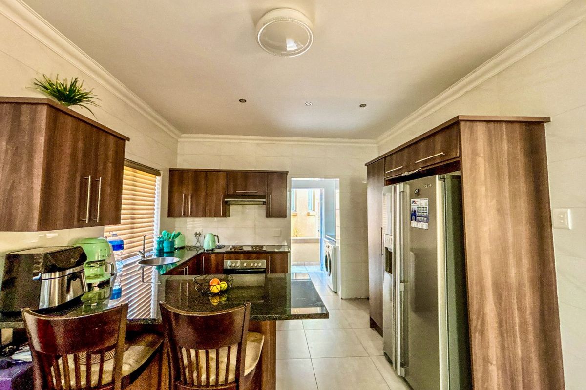 A functional kitchen featuring dark wood cabinetry, granite countertops, built-in appliances, and tiled flooring, with an adjacent laundry area visible.