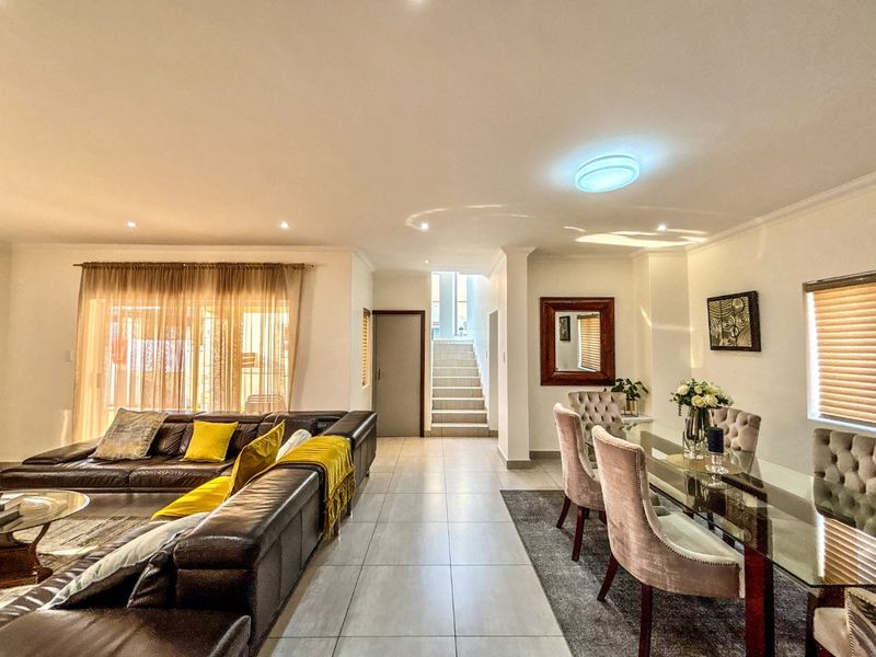 Spacious open-plan living and dining area featuring neutral tiled flooring, recessed lighting, and a central staircase leading to the upper level.