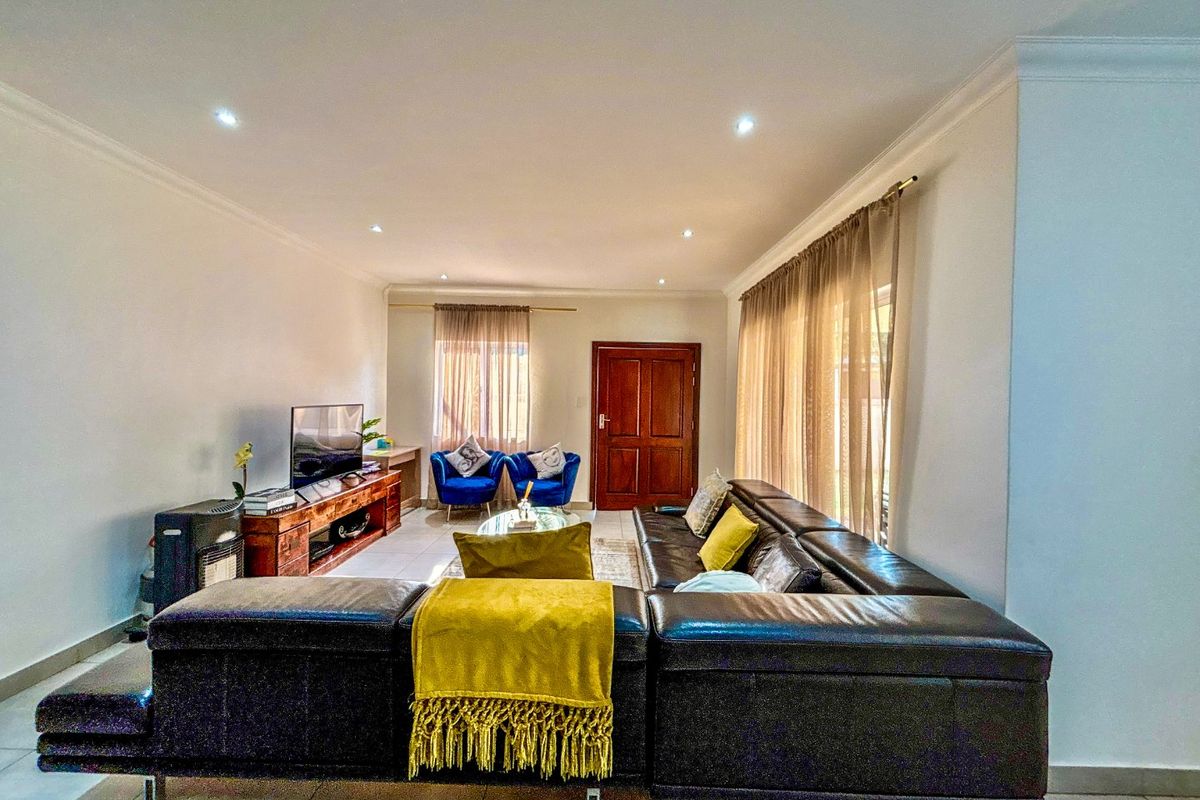 A spacious living room featuring tiled flooring, recessed downlighting, and large windows with curtain tracks, providing a bright and functional living space.
