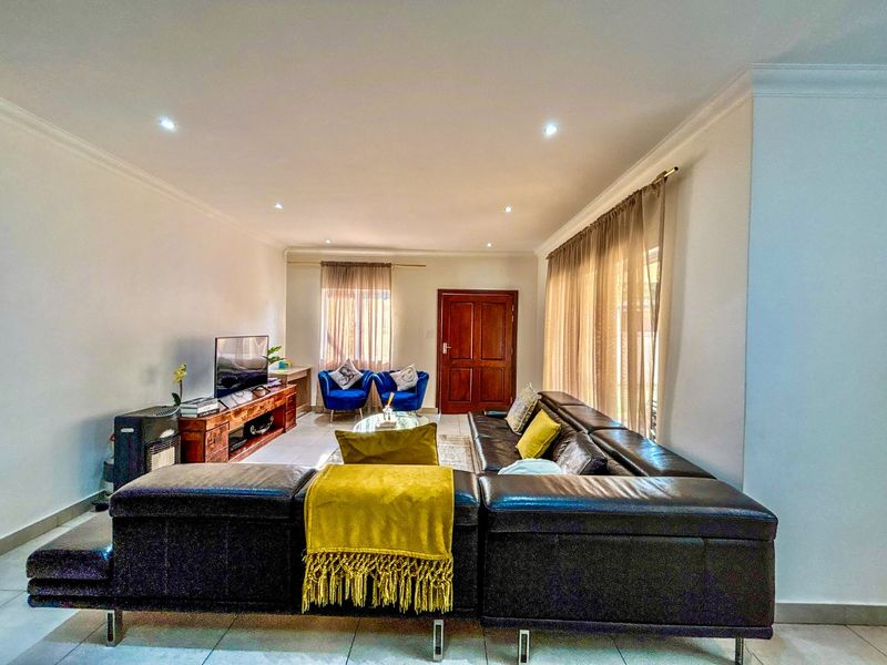 A spacious living room featuring tiled flooring, recessed downlighting, and large windows with curtain tracks, providing a bright and functional living space.