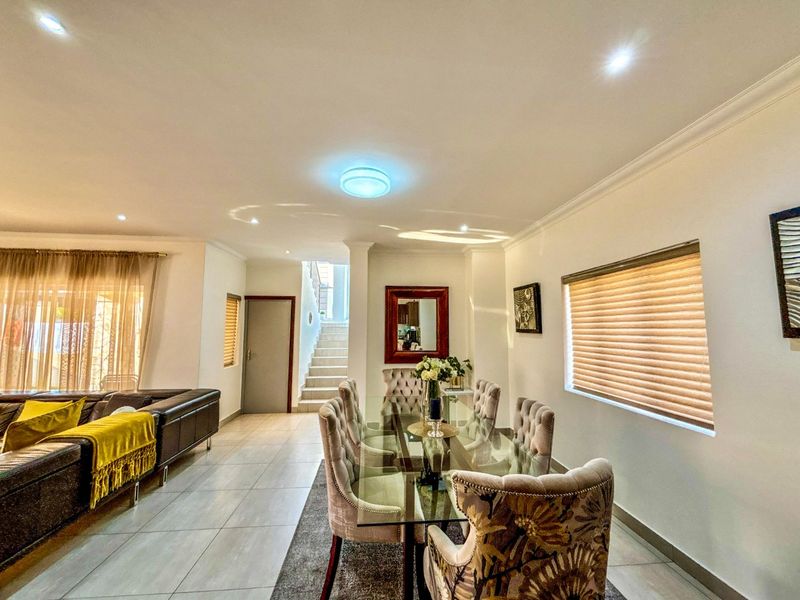 An open-plan living and dining area featuring tiled flooring, recessed lighting, and a staircase leading to the upper level.