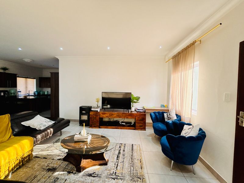 An open-plan living area featuring tiled flooring, recessed downlighting, and a coved ceiling, with a view through to the kitchen area.