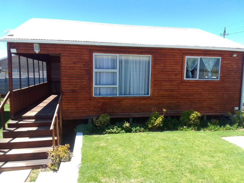 A well-maintained timber-clad commercial building featuring a covered wooden deck, staircase entrance, and large sliding windows set within a landscaped garden area.
