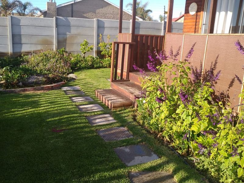A rear garden area featuring a timber deck, stone paver pathway, and a precast concrete boundary wall.