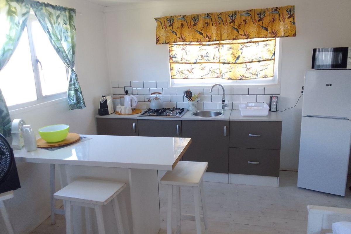 Compact kitchen featuring a gas hob, subway tile backsplash, stainless steel sink, and integrated cabinetry with an attached breakfast bar.