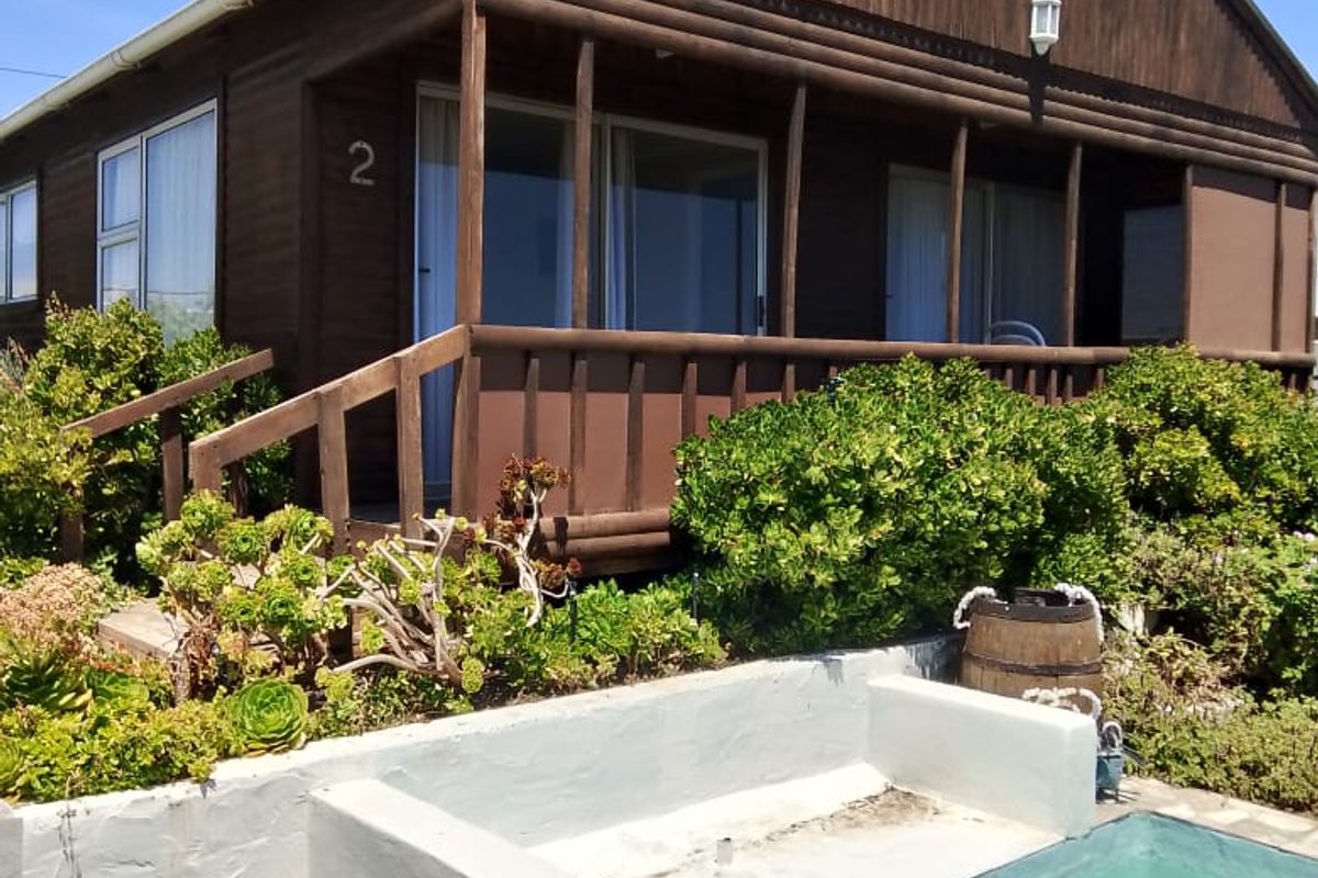 A timber-clad house exterior featuring a covered veranda, a swimming pool, and a landscaped garden area.