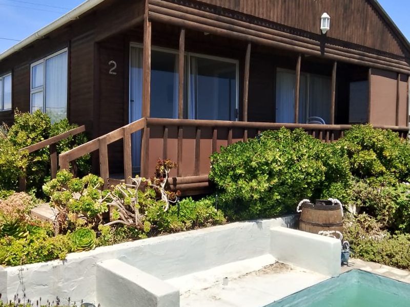 A timber-clad house exterior featuring a covered veranda, a swimming pool, and a landscaped garden area.