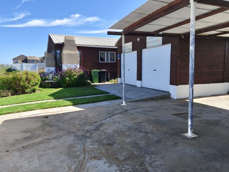 Front exterior view featuring a double garage, attached carport, concrete driveway, and an external fireplace set against a timber-clad building facade.