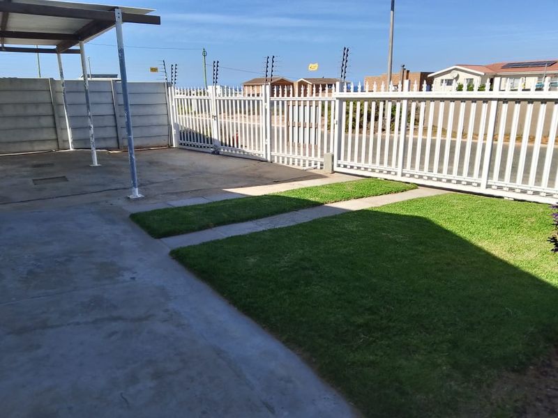 Front exterior area featuring a concrete driveway, lawn, secure metal gate, electric fencing, and a covered carport structure.
