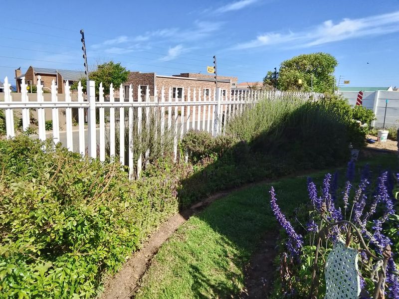 A well-maintained garden area featuring a white picket fence with integrated electric security fencing.