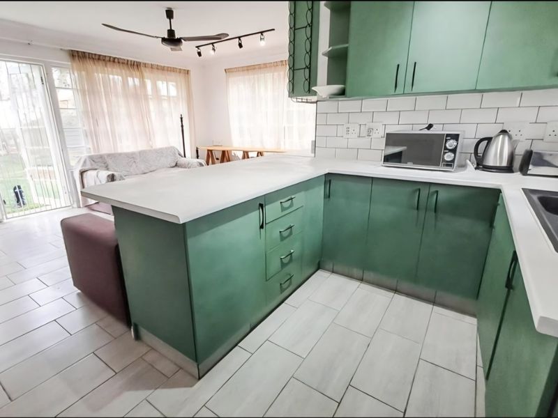 Open-plan kitchen and living area featuring green cabinetry, white subway tile backsplash, tiled flooring, and direct access to the outdoor space via sliding doors.