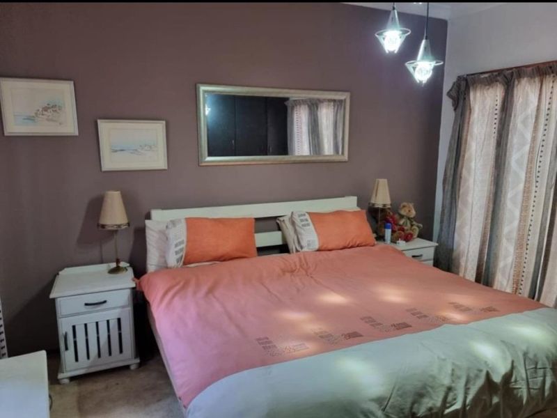 A cozy bedroom featuring a dark accent wall, pendant lighting, and window treatments, providing a comfortable and functional sleeping space.
