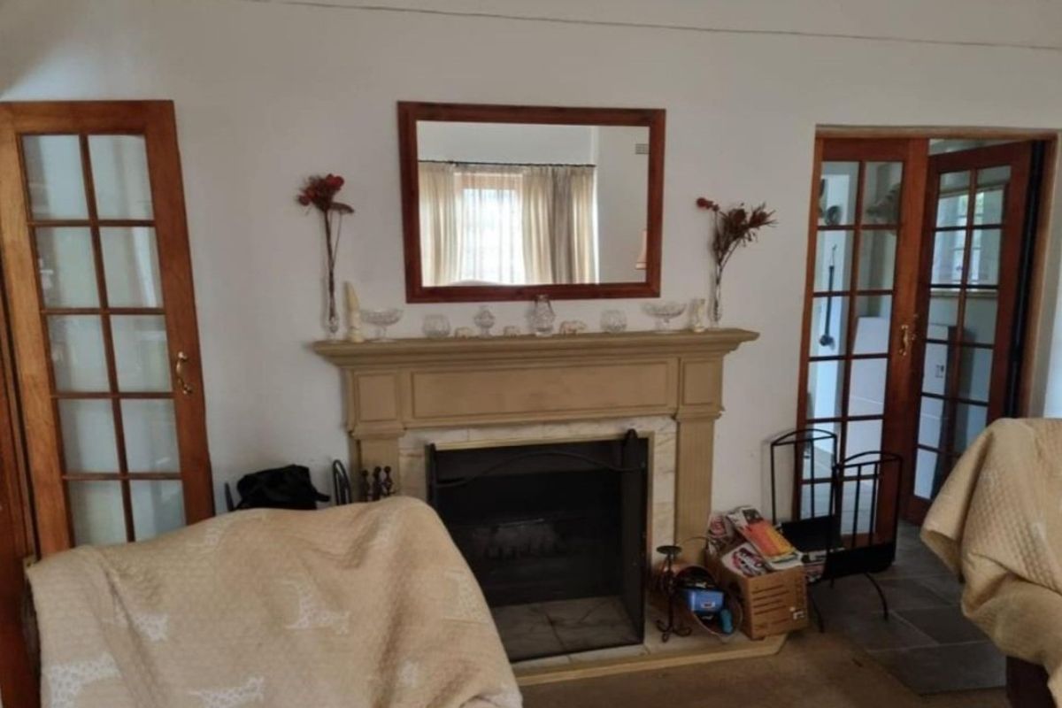 A living room featuring a central fireplace with a mantelpiece, flanked by timber-framed glass doors providing access to adjacent spaces.