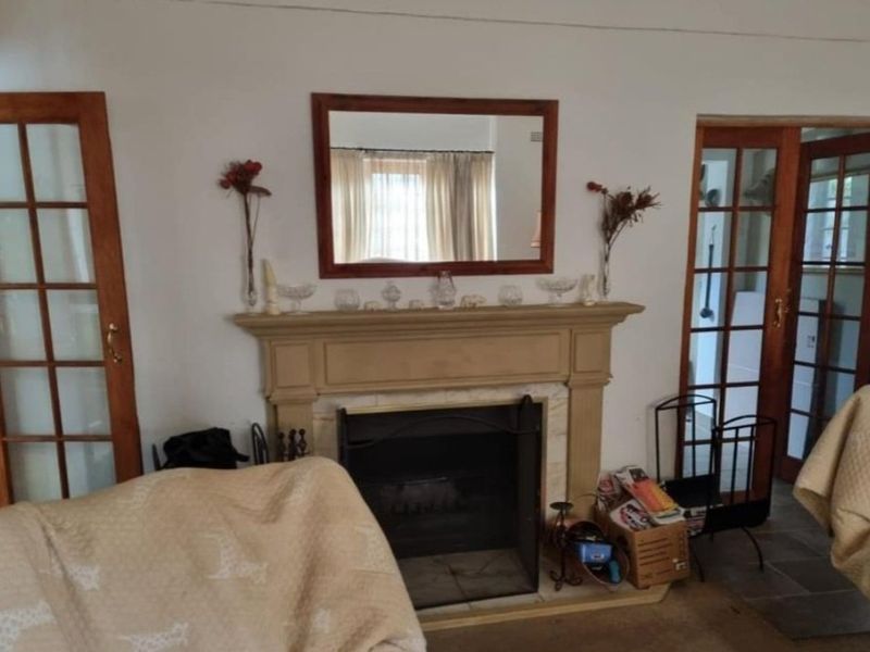 A living room featuring a central fireplace with a mantelpiece, flanked by timber-framed glass doors providing access to adjacent spaces.
