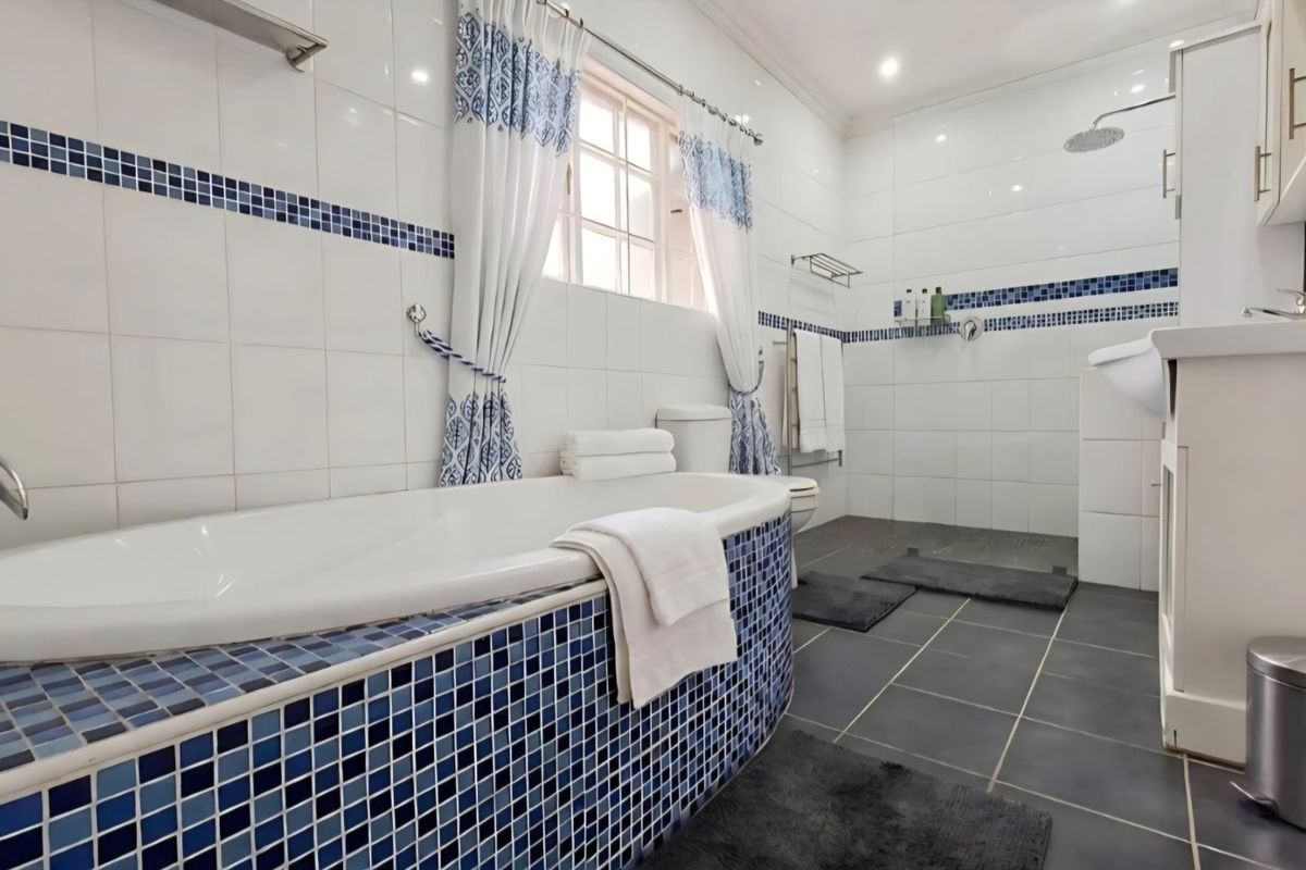 A well-maintained bathroom featuring a built-in bathtub with blue mosaic tiling, a separate shower area, and a vanity cabinet with modern fixtures.