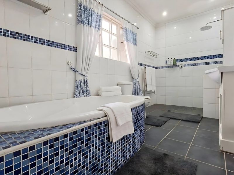 A well-maintained bathroom featuring a built-in bathtub with blue mosaic tiling, a separate shower area, and a vanity cabinet with modern fixtures.