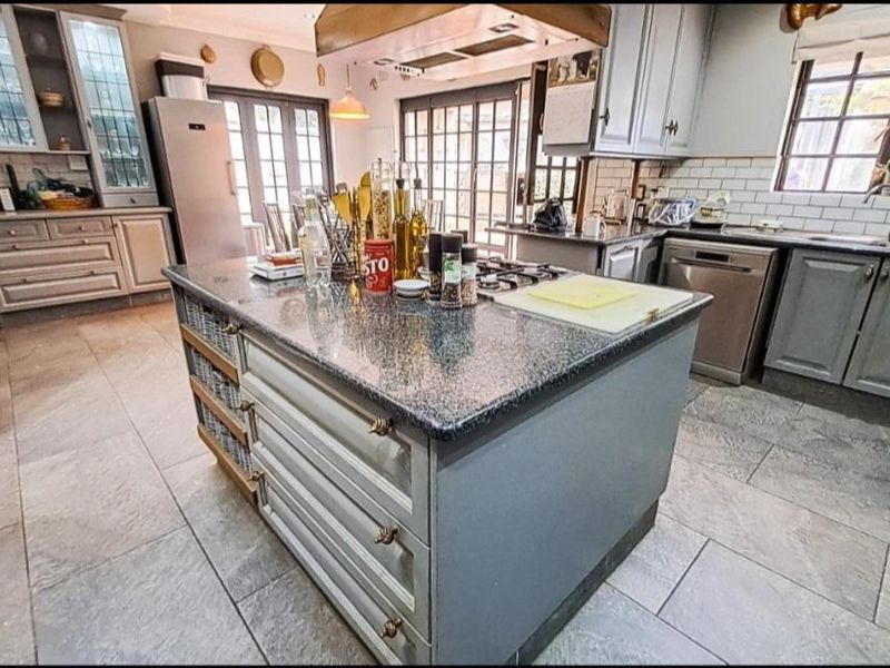 Spacious kitchen featuring a central island with granite countertops, gas hob, ample cabinetry, and stone flooring, opening out through glass doors.