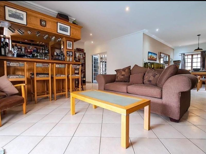 Spacious open-plan living area featuring a built-in wooden bar, tiled flooring, and recessed lighting, creating a versatile space for entertaining.