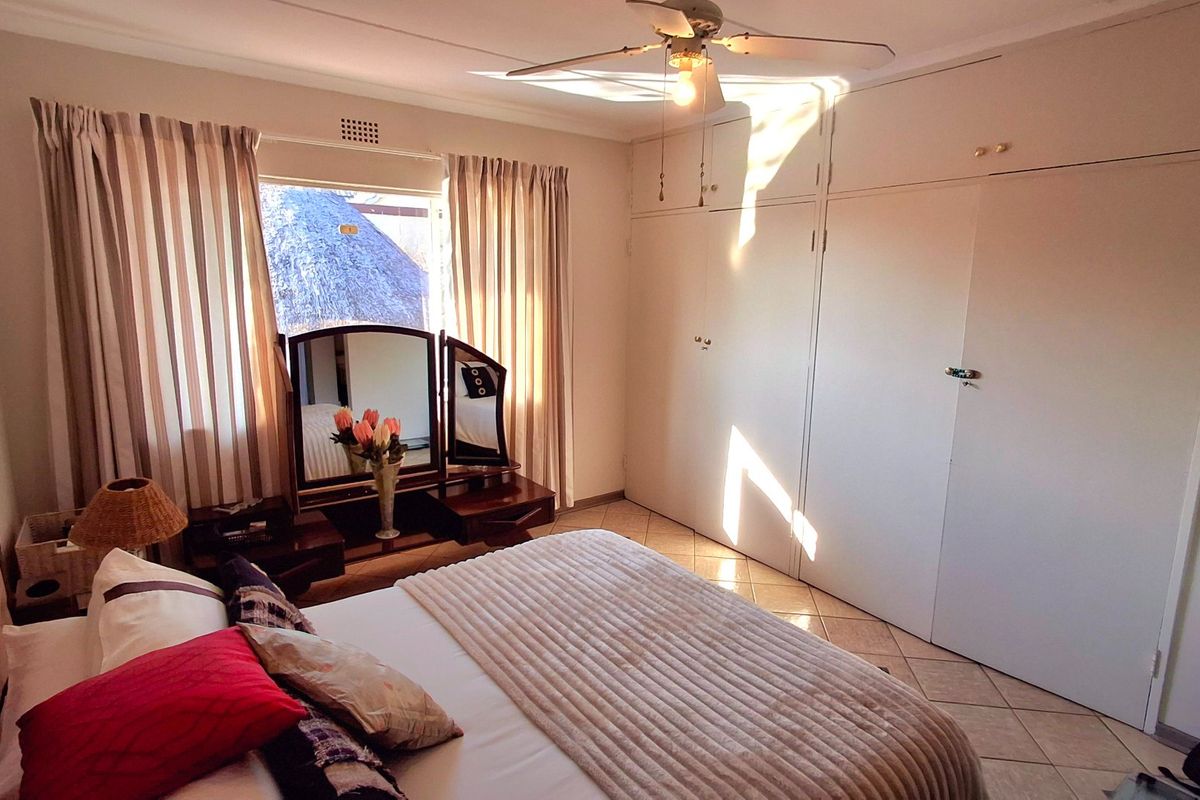 A well-lit bedroom featuring extensive built-in cupboards, tiled flooring, and a ceiling fan, offering a functional and comfortable living space.