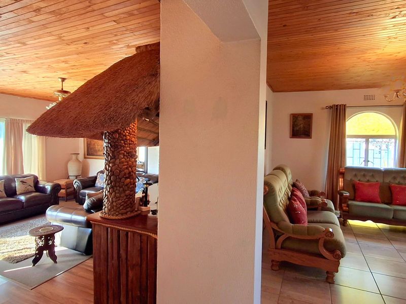 Open plan living area featuring a unique thatched bar, timber ceilings, and a mix of tiled and laminate flooring with natural light.