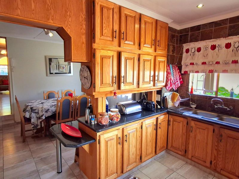 A functional kitchen featuring traditional wooden cabinetry, granite countertops, a double basin sink, and a tiled backsplash, with an adjacent dining area.