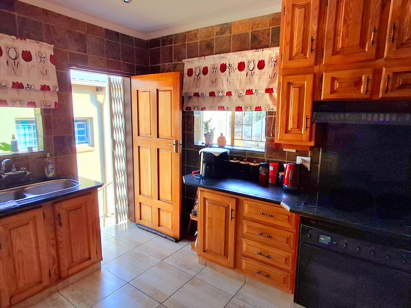A functional kitchen featuring wooden cabinetry, black granite countertops, a double sink, and built-in appliances with direct access to the exterior.