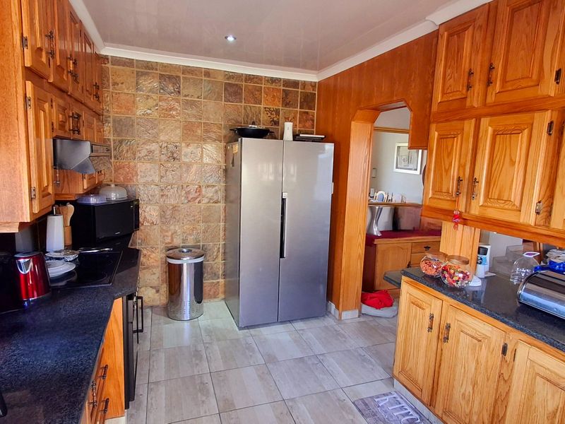 A functional kitchen featuring extensive wooden cabinetry, stone tile backsplash, and dark countertops, offering a traditional aesthetic with ample storage space.