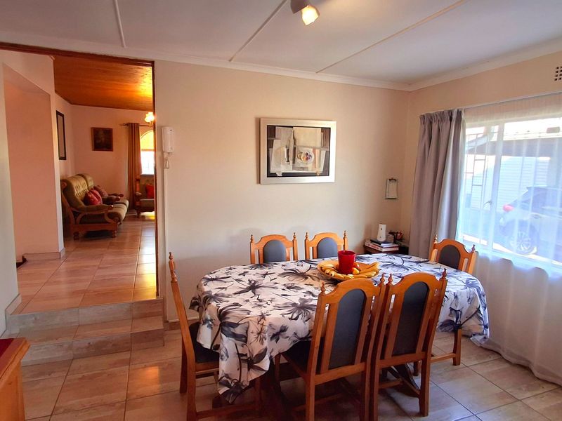 A functional dining room featuring tiled flooring, coved ceilings, and a large window, with an open transition to the adjacent living area.
