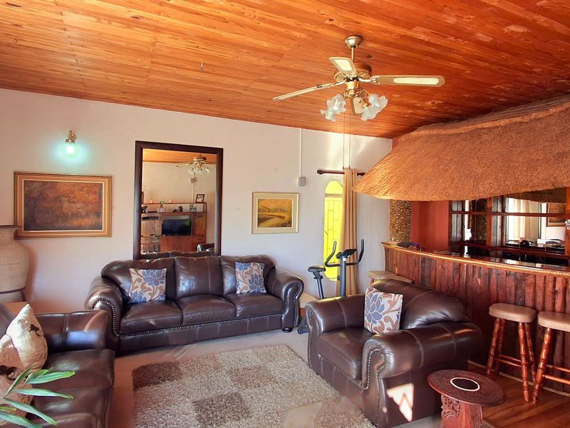 A living room featuring a timber-clad ceiling, ceiling fan, and a built-in bar area with a traditional thatch canopy.