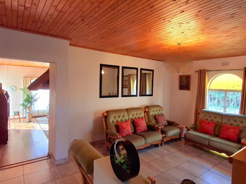 A spacious living room featuring a warm timber tongue and groove ceiling, ceramic tiled flooring, and an arched window allowing natural light.