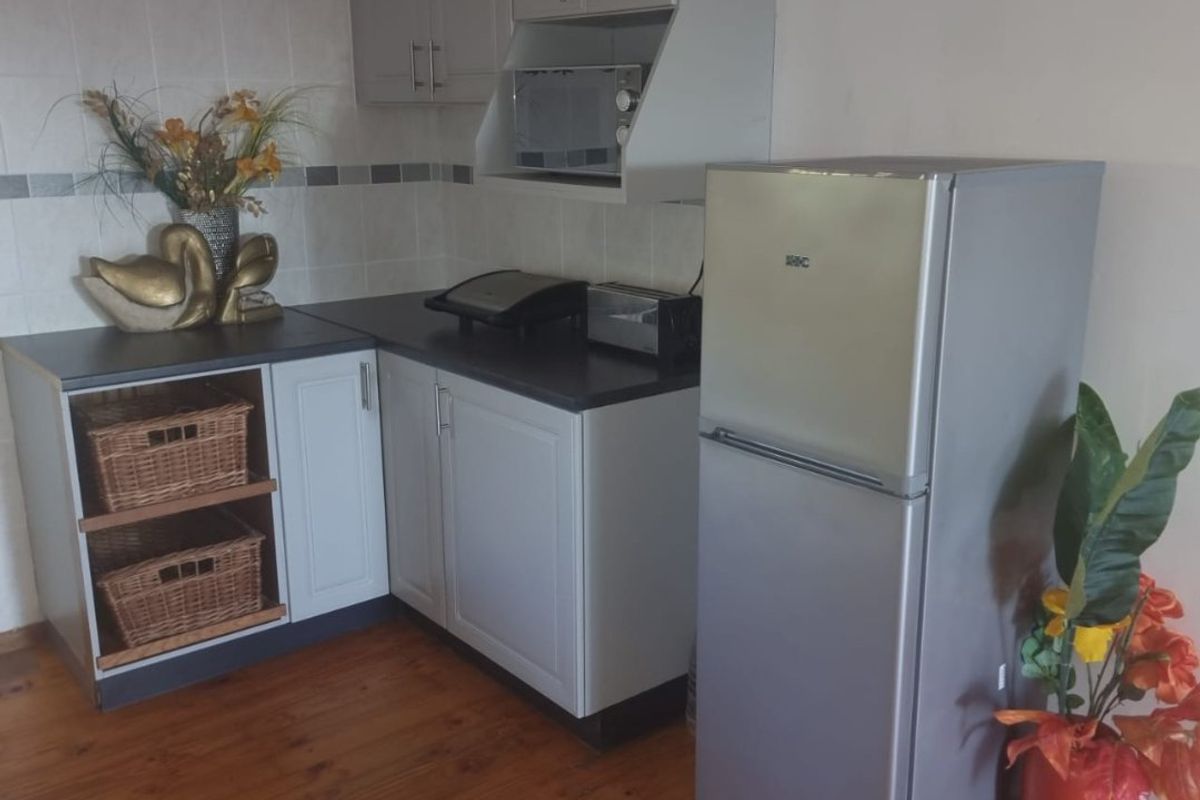 A compact kitchen area featuring grey built-in cabinetry, dark laminate countertops, tiled backsplash, and timber flooring.