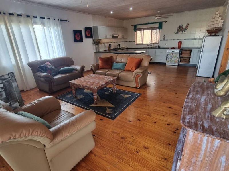 Spacious open-plan living area featuring warm timber flooring, a ceiling fan, and a functional kitchen with tiled backsplash and ample cabinetry.