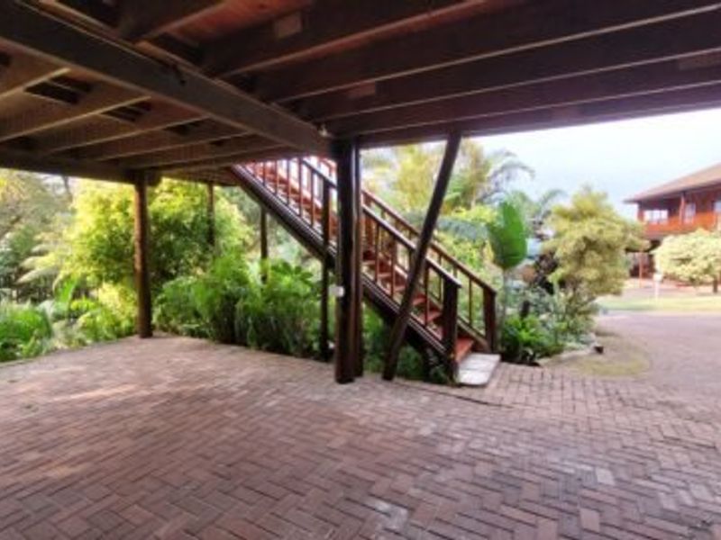 A covered outdoor parking area featuring brick paving and a timber staircase leading to the upper level of the property.