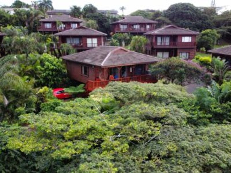 An aerial view of a residential complex featuring multiple timber-clad units with tiled roofs set within a lush, mature garden environment.