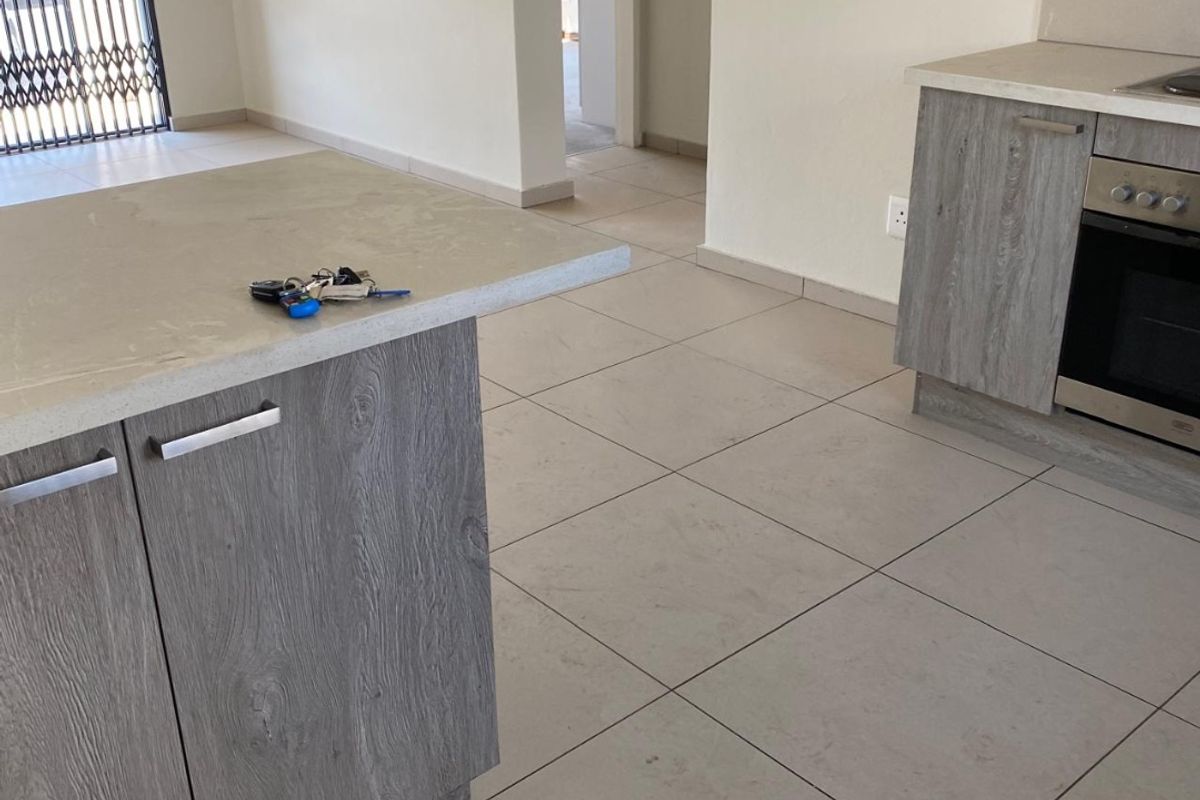 Modern kitchen featuring grey wood-grain cabinetry, stone countertops, and a built-in oven, set against neutral tiled flooring in an open-plan layout.
