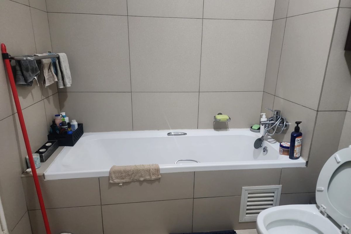 A functional bathroom featuring a built-in bathtub with wall-mounted mixer and neutral wall tiling.