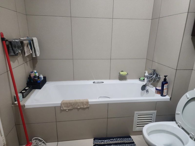A functional bathroom featuring a built-in bathtub with wall-mounted mixer and neutral wall tiling.