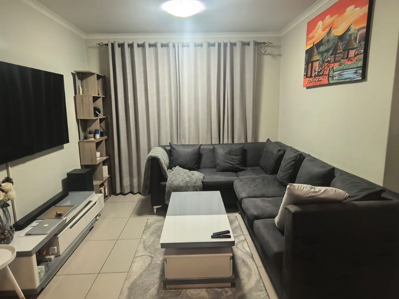 A well-maintained living room featuring neutral tiled flooring, cove cornicing, and a central ceiling light fixture, providing a comfortable and functional living space.