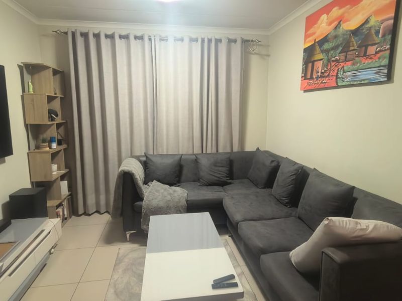 A comfortable living room featuring neutral tiled flooring, coving, and large window treatments, providing a functional and well-maintained space for relaxation.