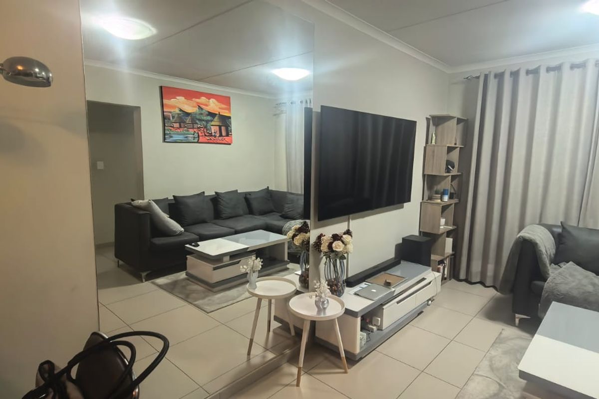 A well-maintained living room featuring tiled flooring, a large mirrored wall feature, and neutral wall finishes, providing a bright and functional living space.
