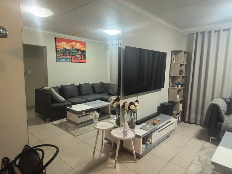 A well-maintained living room featuring tiled flooring, a large mirrored wall feature, and neutral wall finishes, providing a bright and functional living space.