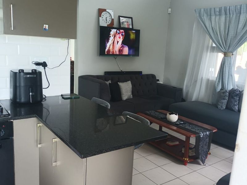 Open-plan living area featuring a modern kitchen with granite countertops and tiled flooring, seamlessly flowing into a comfortable lounge space with high ceilings.