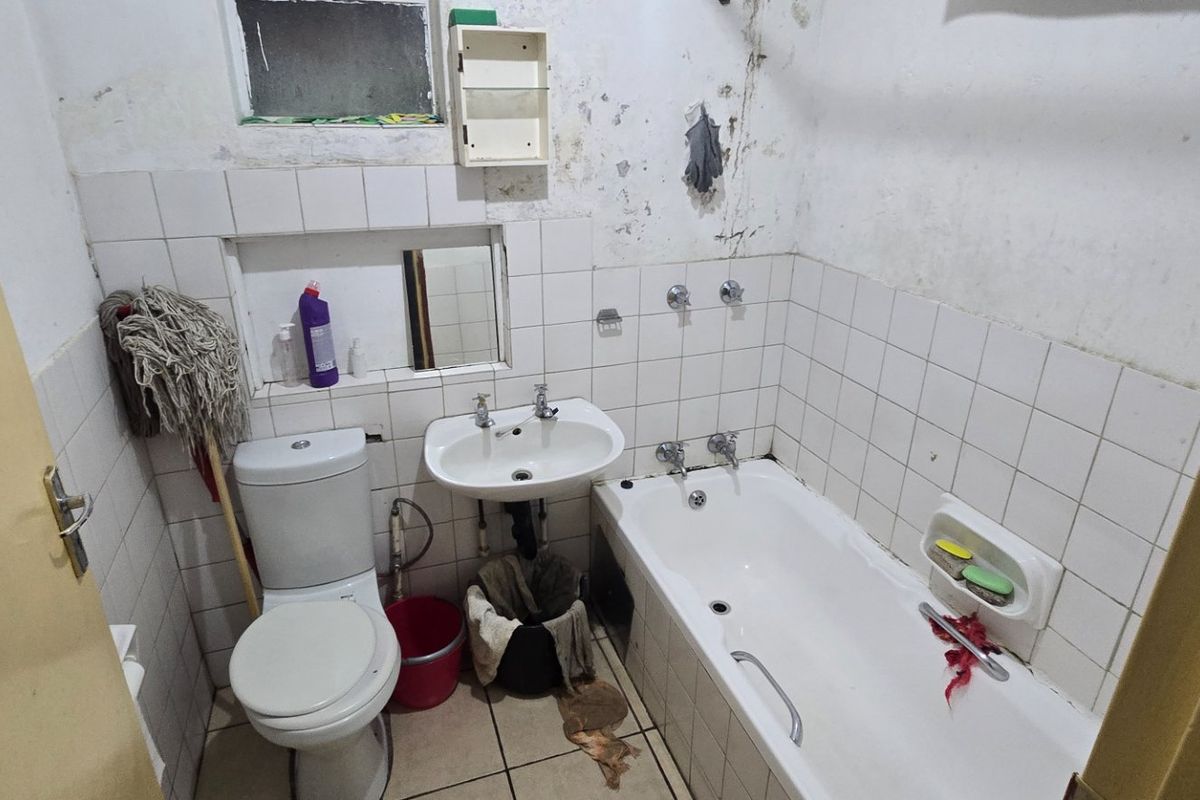 A compact bathroom featuring a bathtub, pedestal basin, and toilet, requiring significant cosmetic renovation and wall surface repairs.