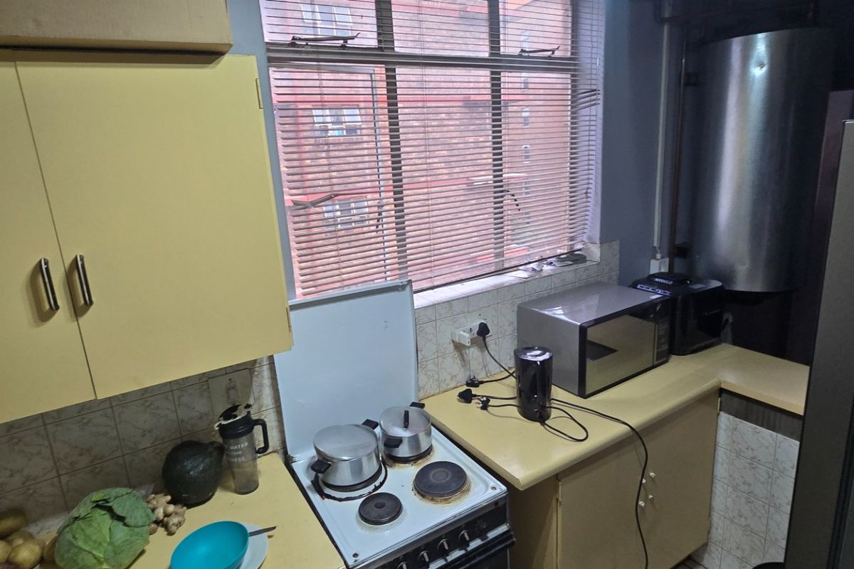 A compact kitchen featuring dated cabinetry, a built-in electric stove, tiled backsplash, and a geyser, offering potential for a modern renovation.