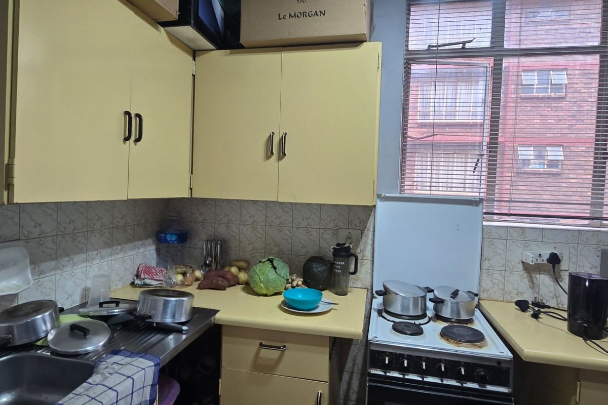 A compact kitchen featuring dated cabinetry, laminate countertops, a stainless steel sink, and a freestanding stove with tiled backsplash.