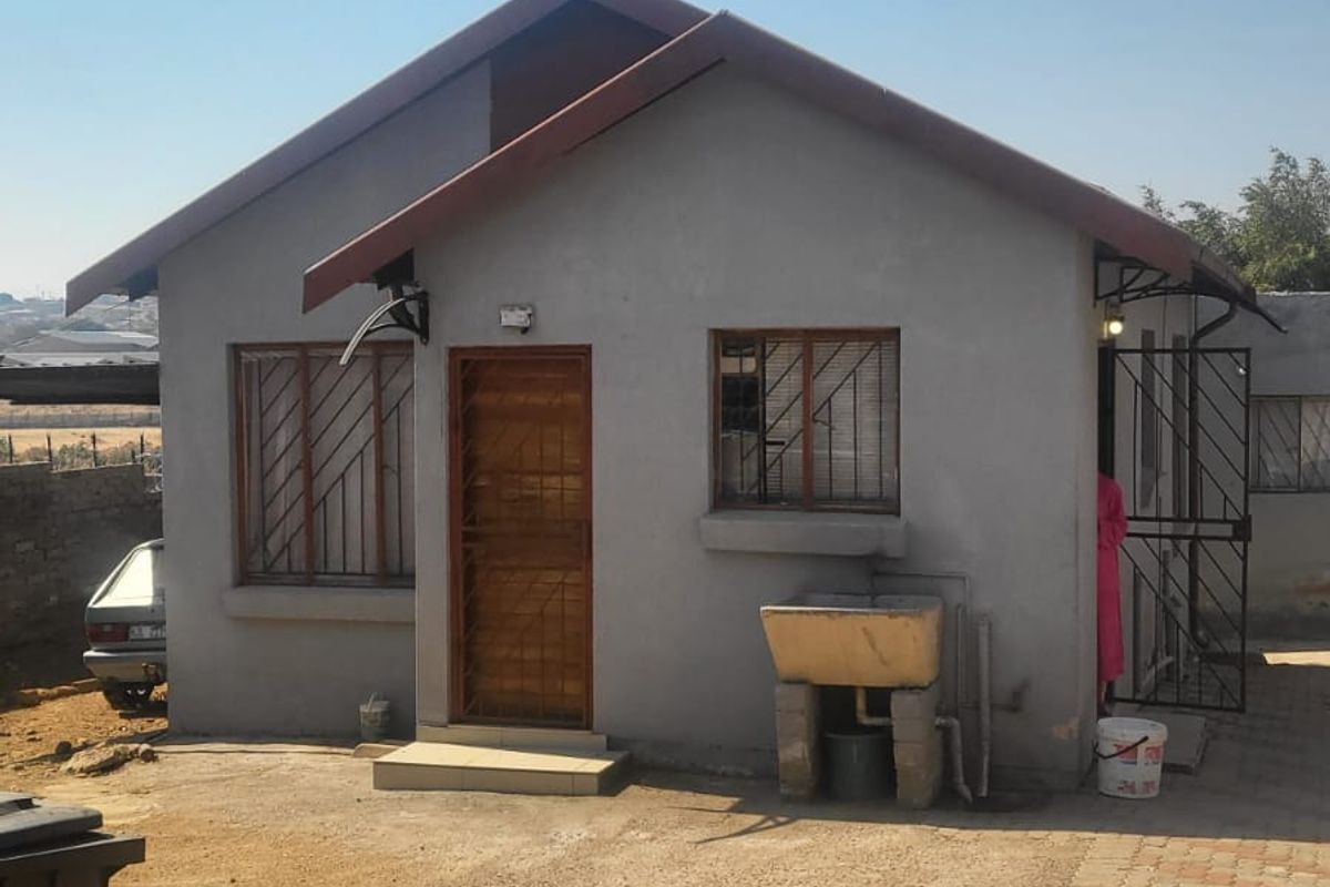 Rear view of a modest detached house featuring a pitched roof, security gates, burglar bars, and an external laundry wash trough.