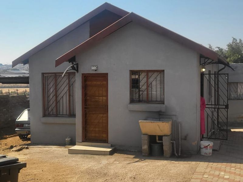 Rear view of a modest detached house featuring a pitched roof, security gates, burglar bars, and an external laundry wash trough.